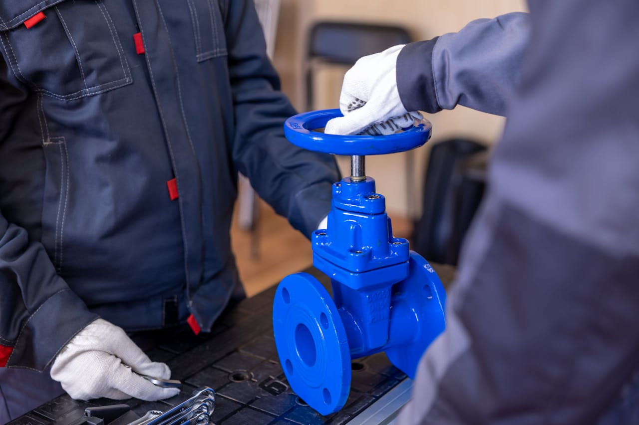Close-up of two technicians adjusting a blue industrial valve indoors.